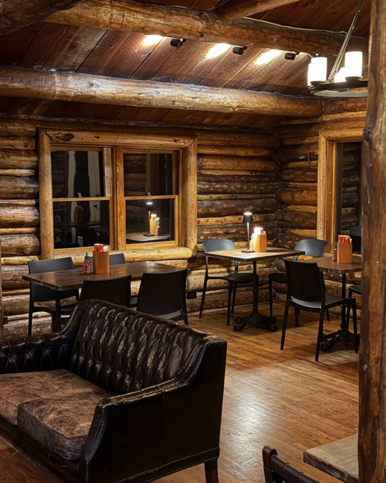 The TYGR Mart dining room at night: log walls, a tufted leather sofa, and tables under warm ceiling lights